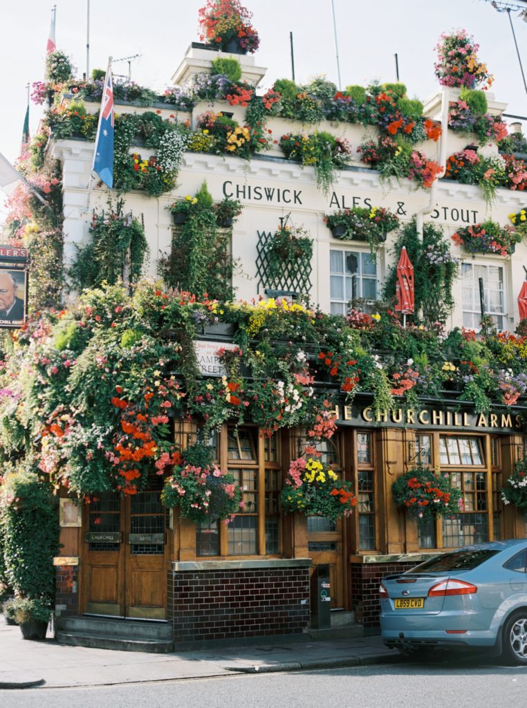 the exterior of churchills arms, a building covered in bright flowers and plants